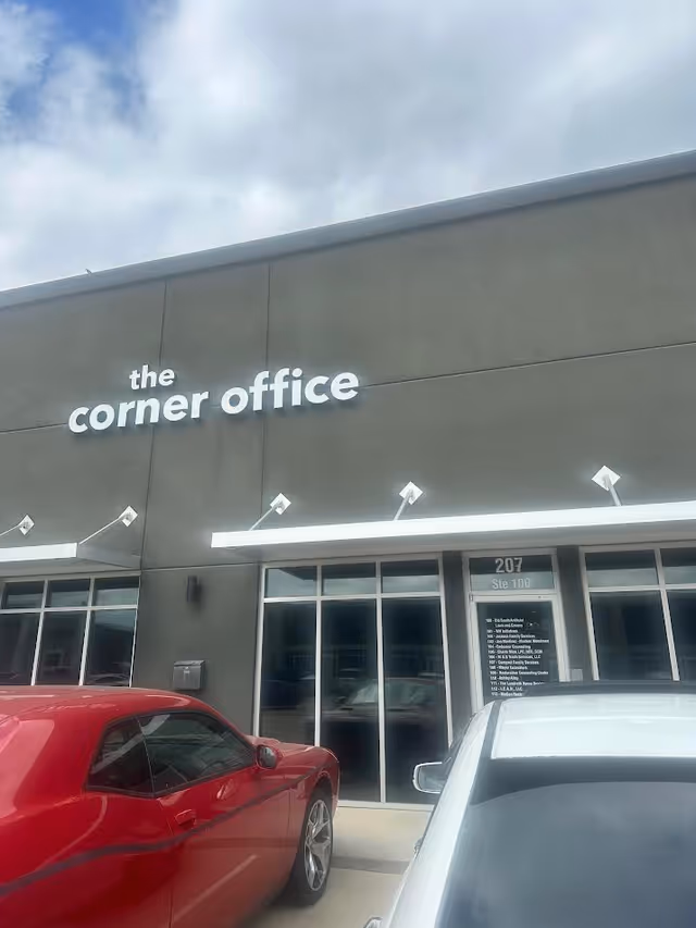 Exterior view of a building with glass storefront, the corner office sign, and parked cars.