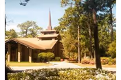 Exterior view of a building with a pointed spire, trees, and landscaped entrance.