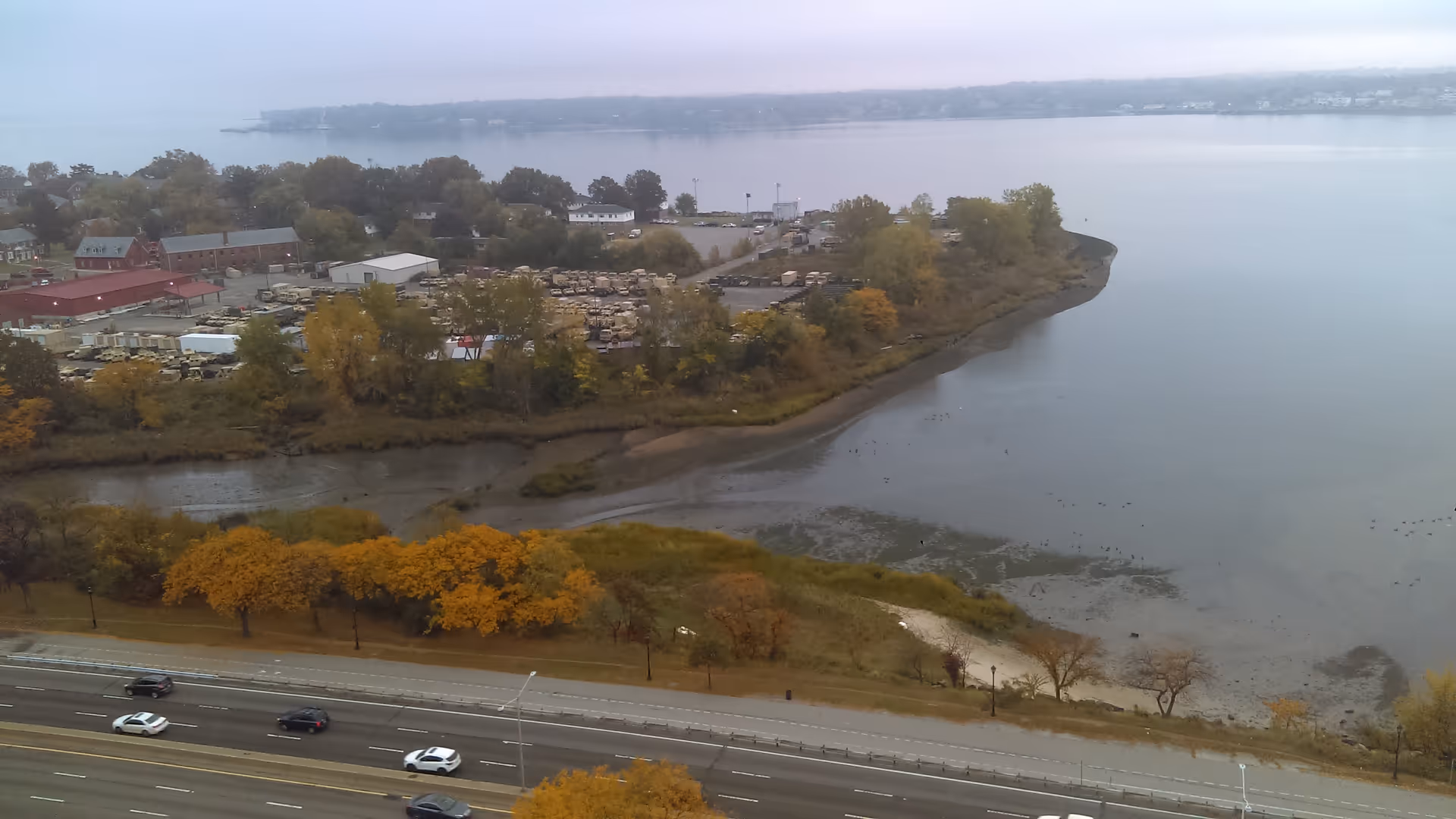 Aerial waterfront scene showing a peninsula with fall trees and a highway.