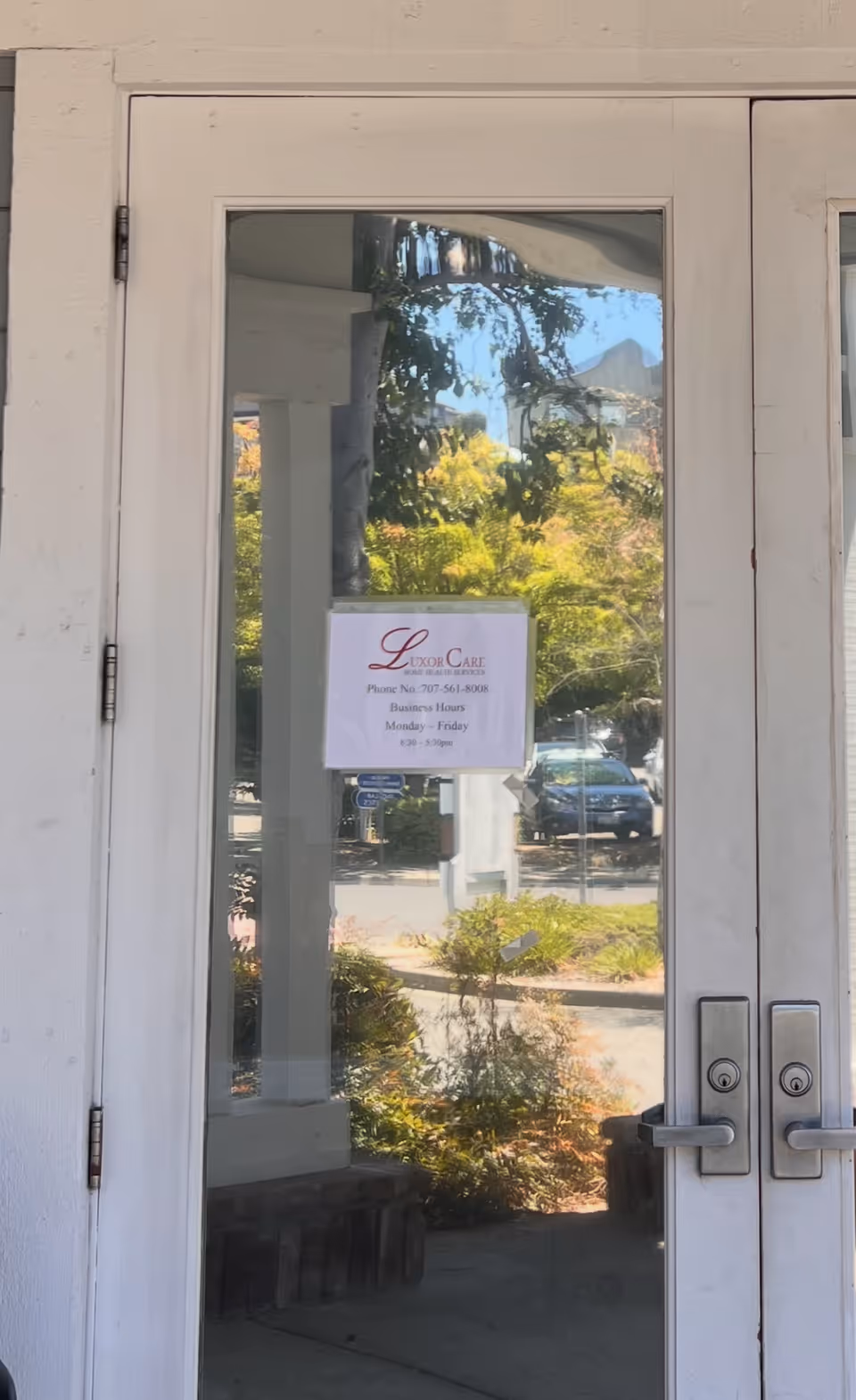 Glass front door with a Luxor Care Home Health Services sign and landscaping outside.
