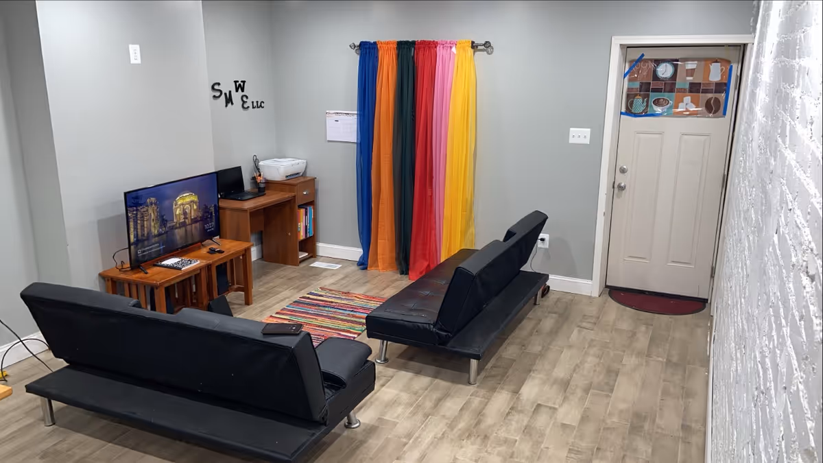 A cozy living room with black leather sofas, a TV on a stand, and colorful curtains.