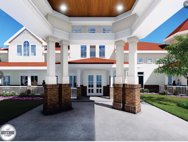 Front entrance portico of a white, red-roofed senior living building with brick-column bases and landscaped walkways.