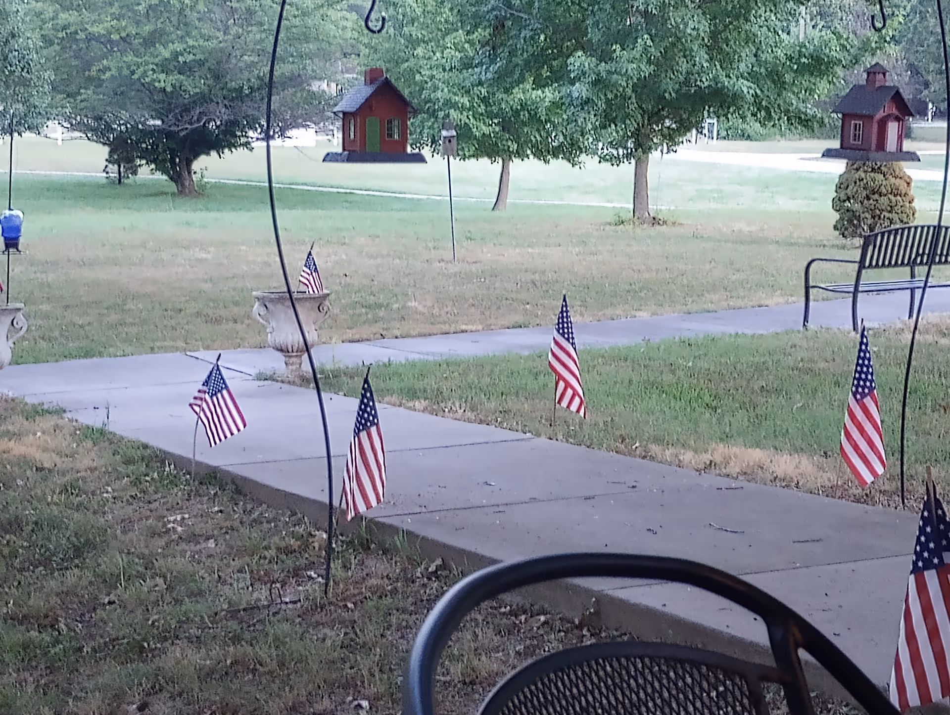Outdoor garden area with flags along a sidewalk and birdhouses, empty benches visible.