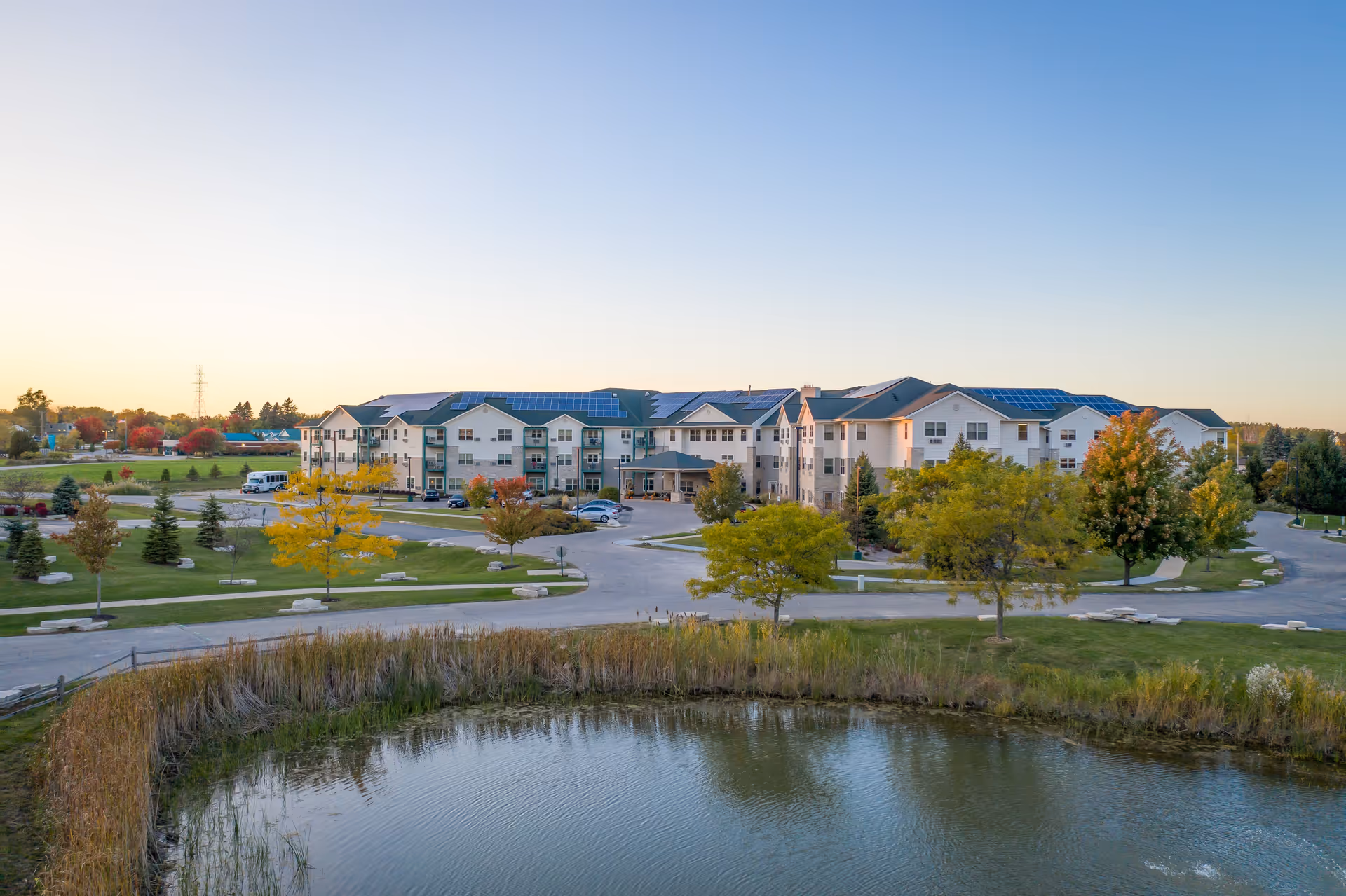 Exterior view of a senior living campus with a pond, trees, and a multi-building complex