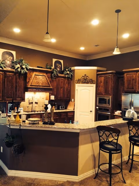 Warm wooden cabinets frame a granite kitchen island with bar stools in a senior living facility.