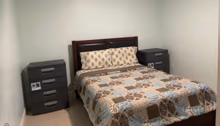 A neatly made bed with matching nightstands sits in a small, plain bedroom.