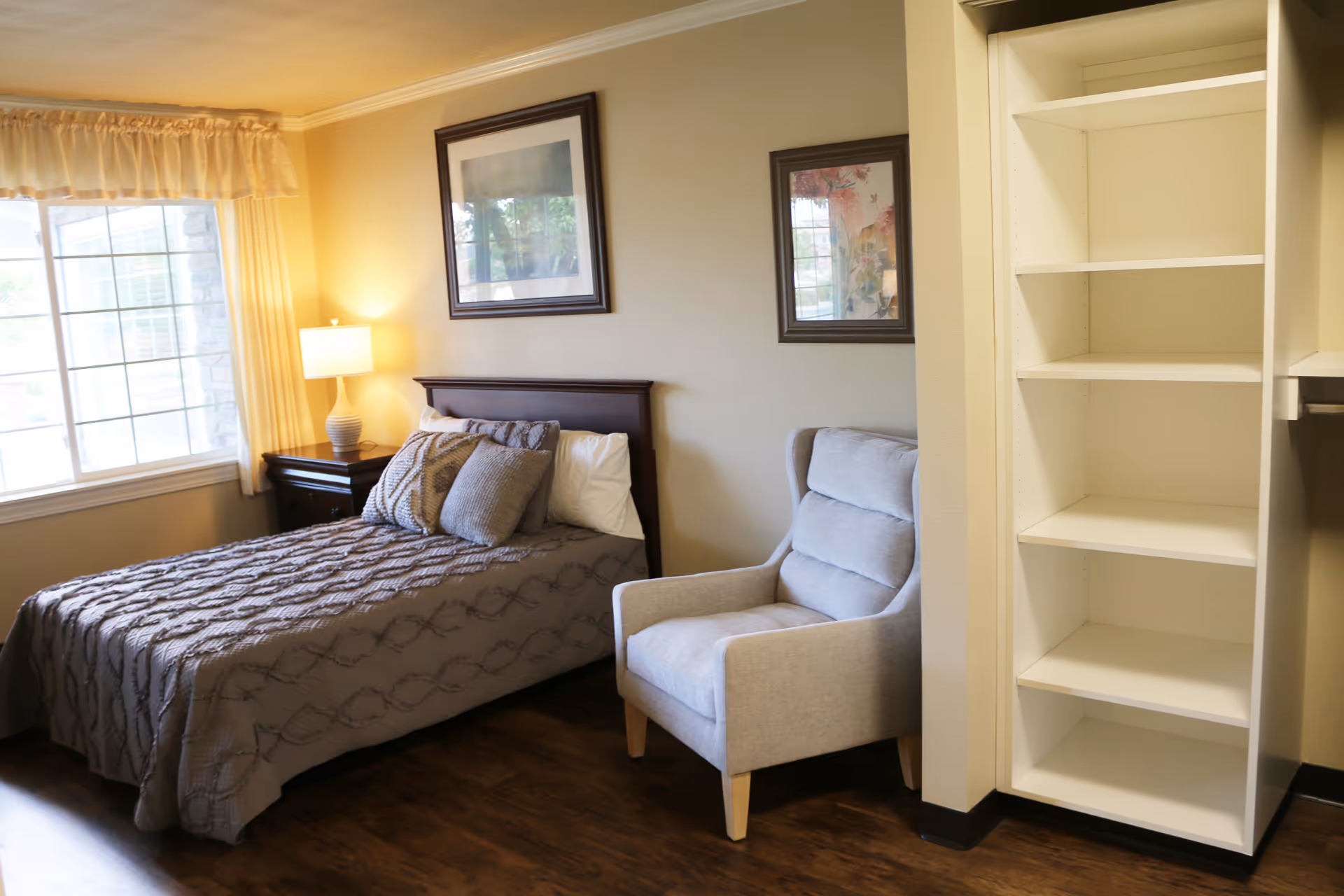 Cozy bedroom in Aspen Ridge Alzheimer’s Special Care Center with bed, chair, and open closet shelving.