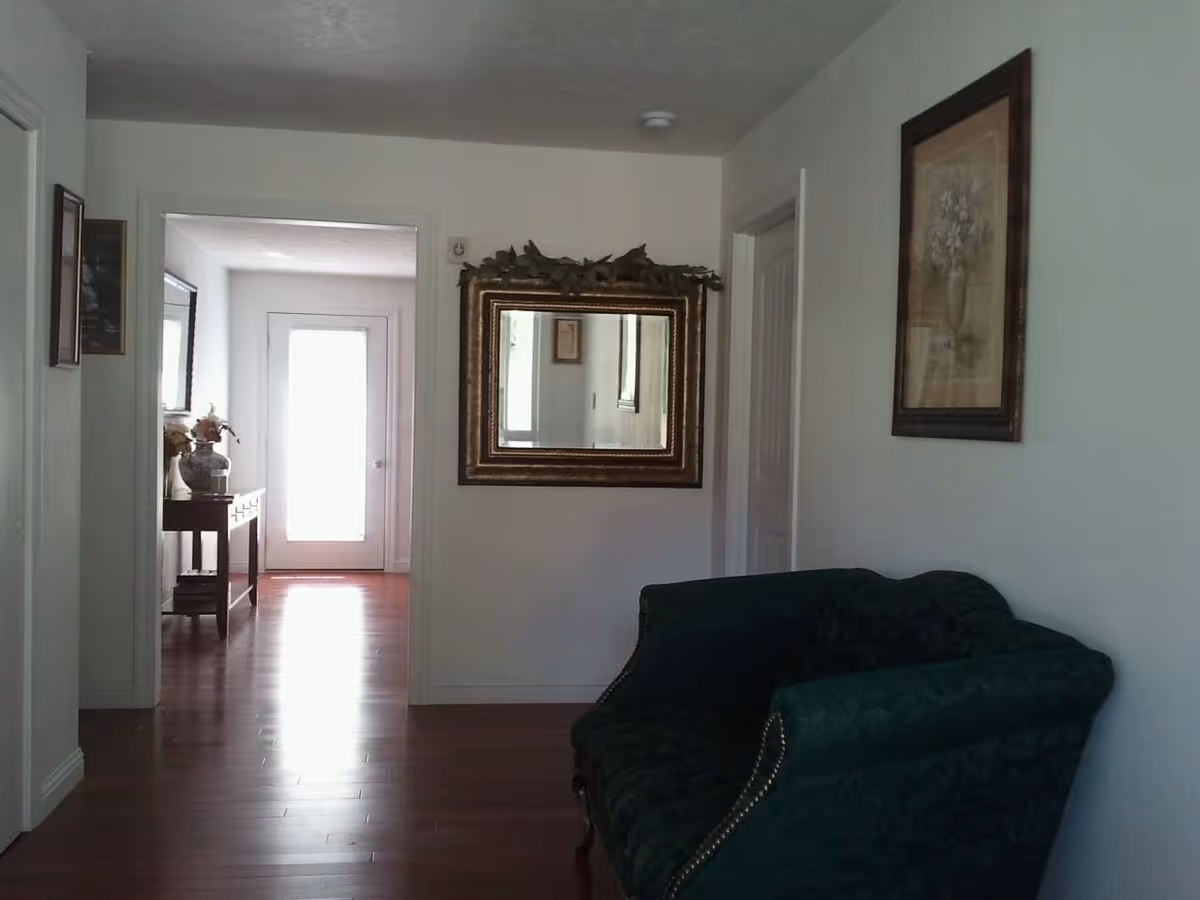 Dim hallway interior with a green sofa, framed art, and a decorative mirror.