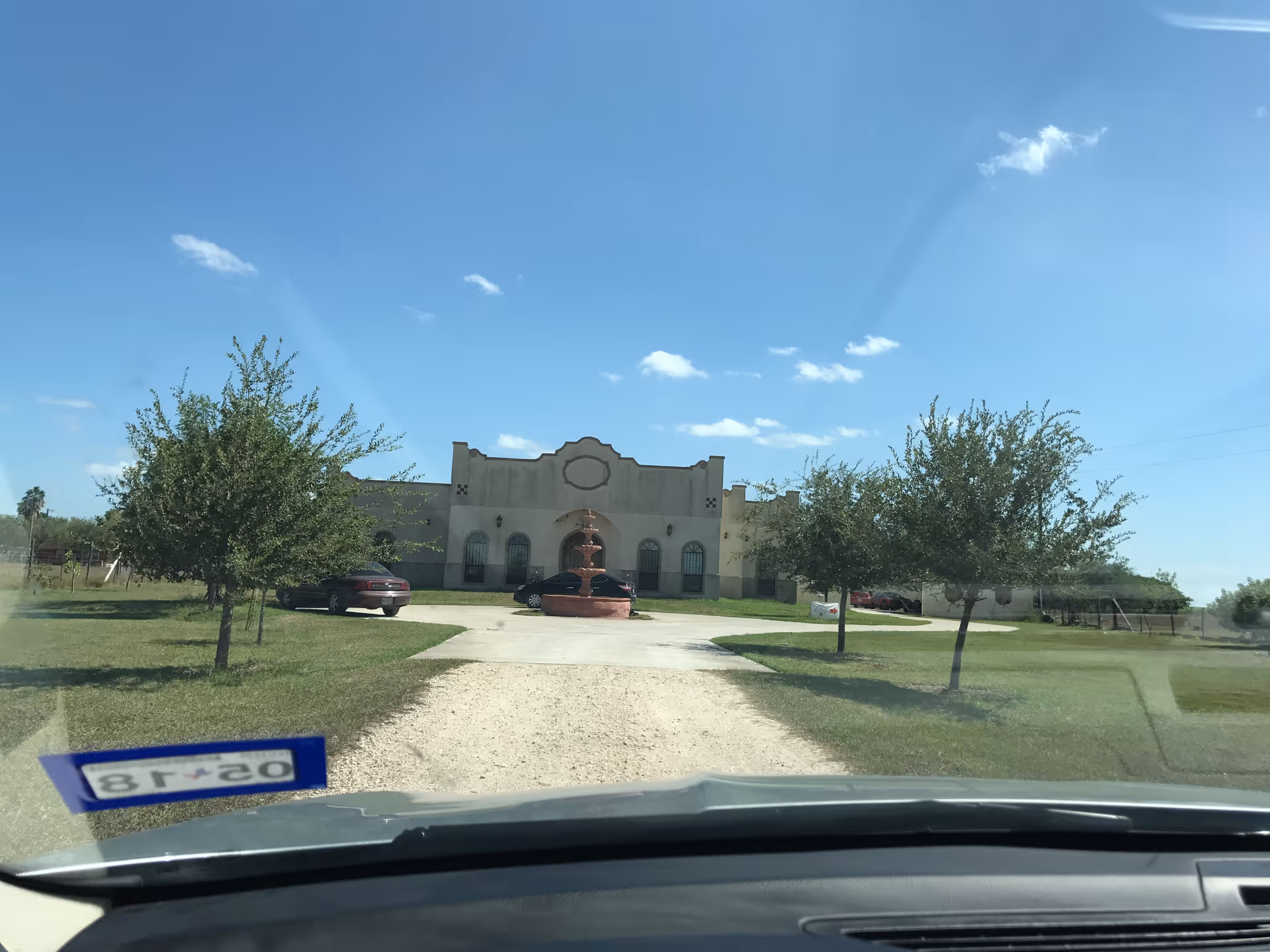 Front view of Hacienda Health Care building with driveway, fountain, trees, and clear blue sky.