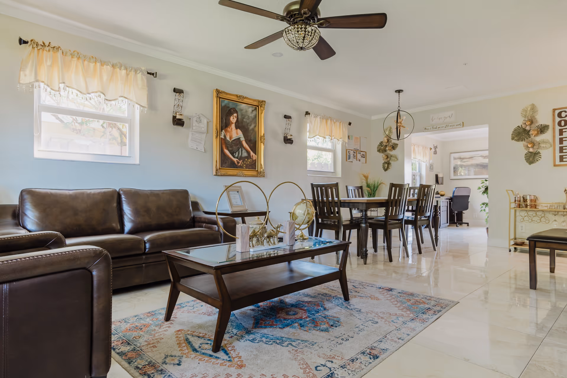 Bright senior living common area with leather sofas, a glass coffee table, and a dining table in a well-lit room.