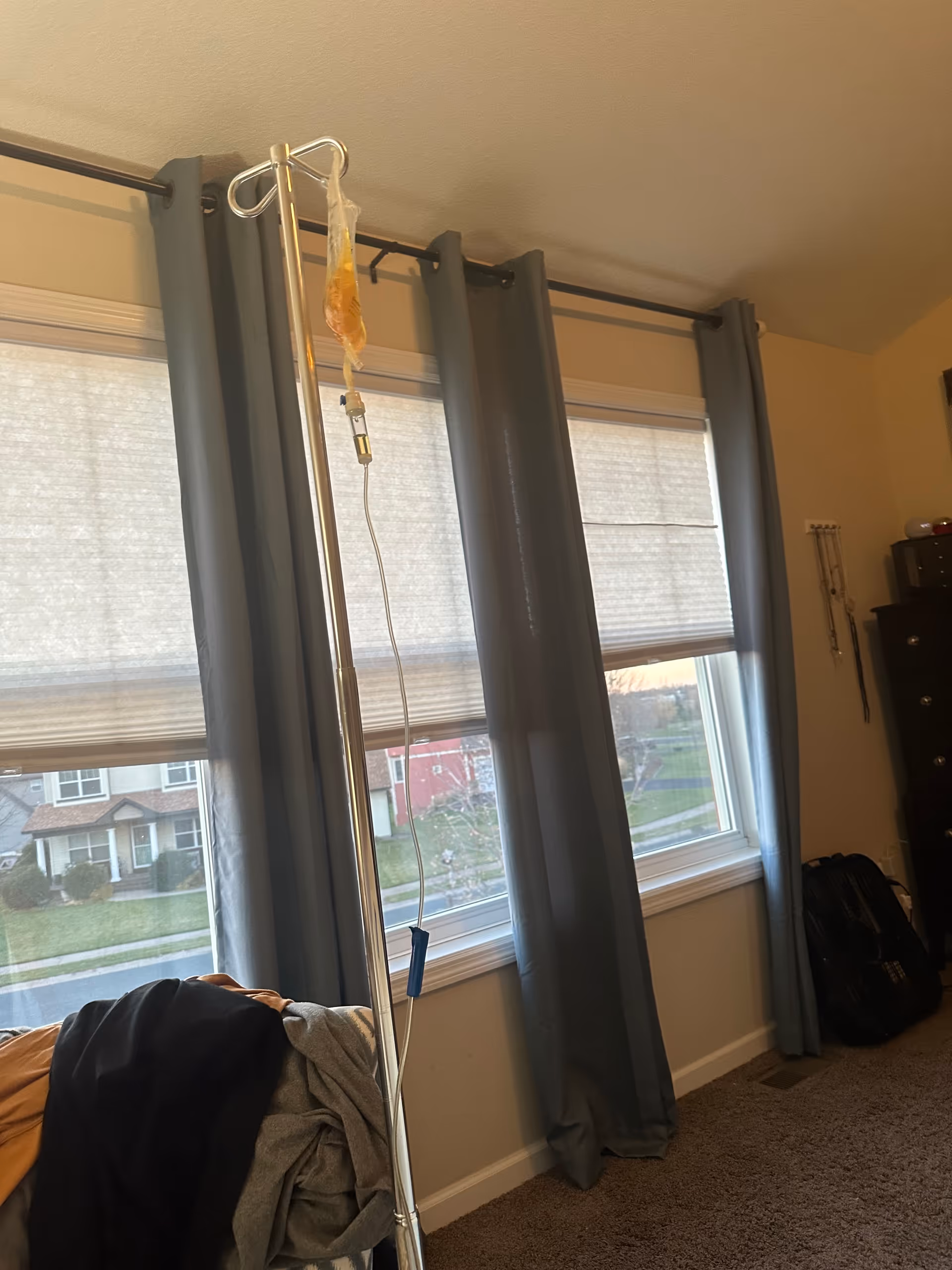 IV infusion stand in a bedroom beside blue-curtained windows.