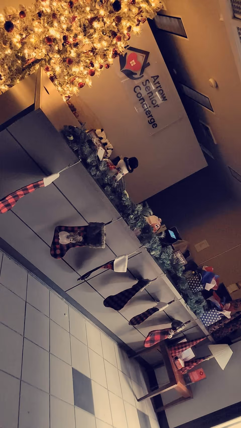 Indoor hallway with holiday garlands, stockings, and an Arrow Senior Concierge sign.