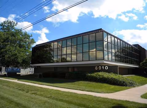 Glass-front senior living facility with large windows, manicured lawn, and a sidewalk.