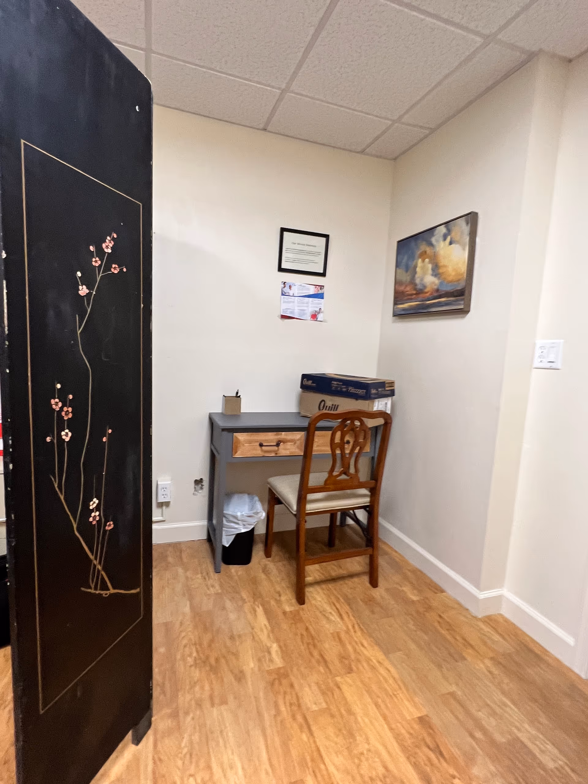 Small office nook with desk, chair, trash can, and decorative cherry-blossom screen.