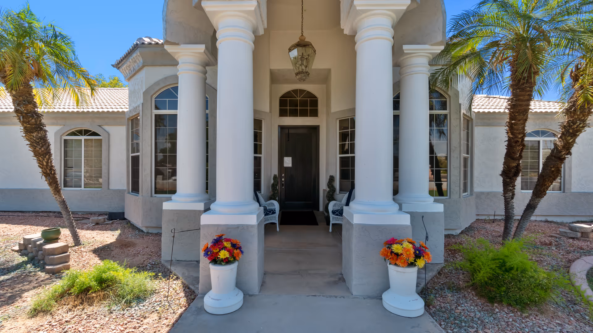 Front view of a senior living facility entrance with columns, steps, and potted flowers.