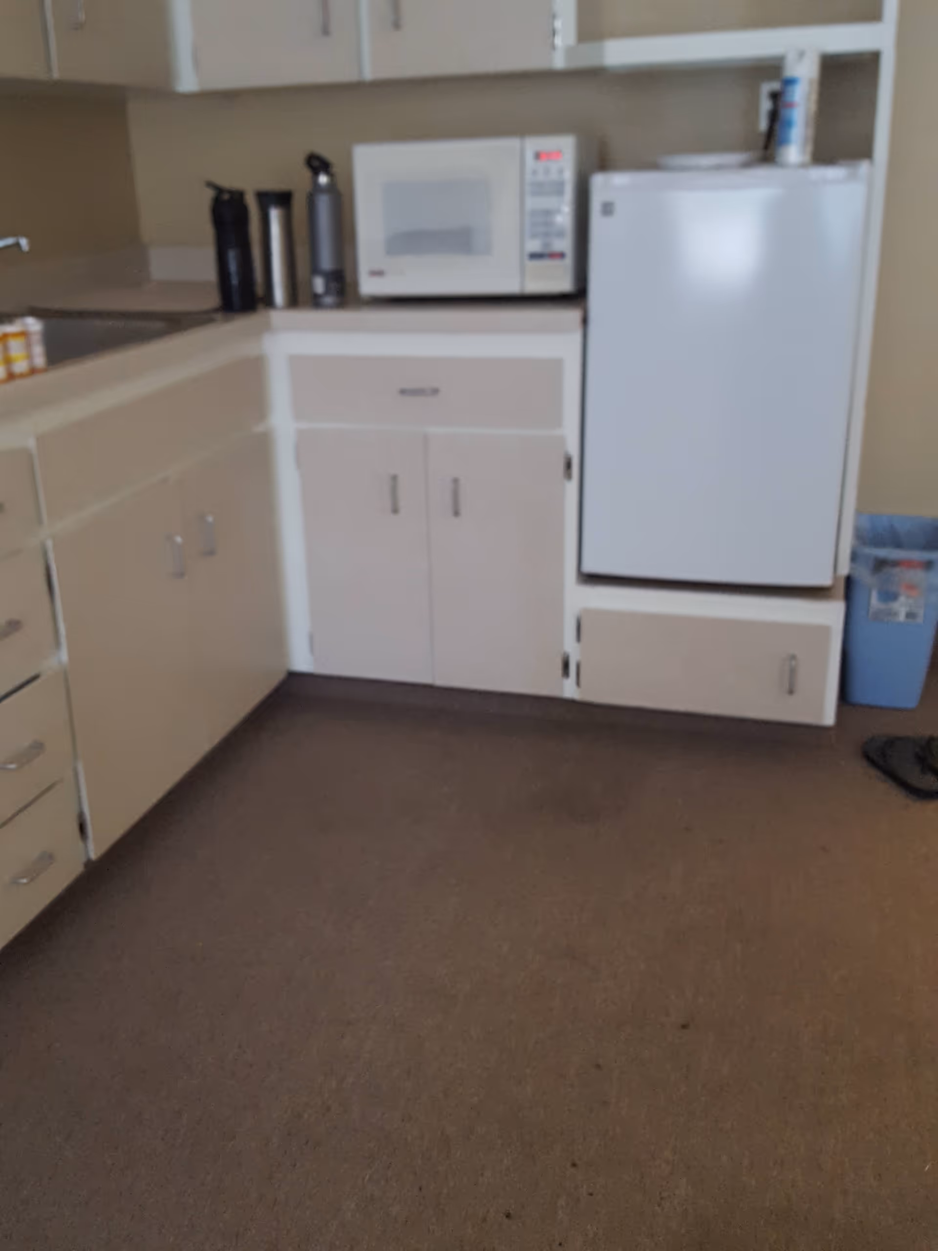 Compact kitchen area with microwave, fridge, and cabinets in a senior living facility.