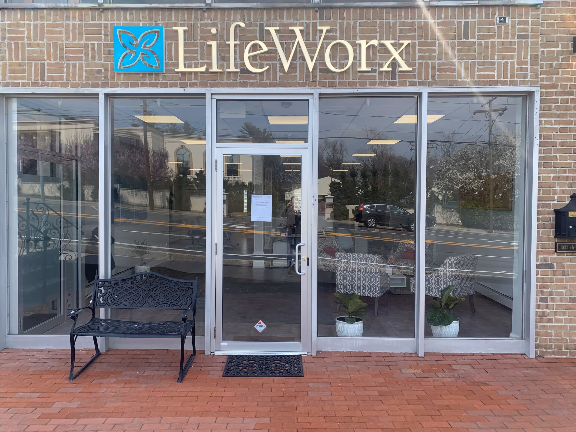 Exterior view of LifeWorx Home Care entrance with glass doors and a bench outside.