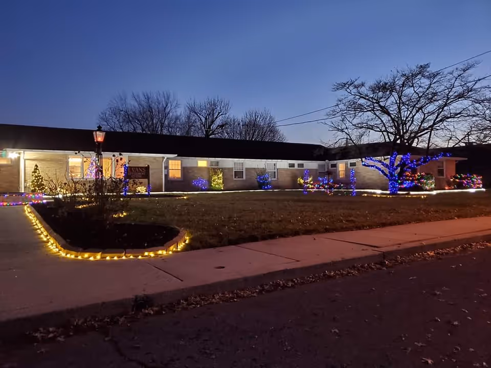 Single-story Evans Retirement Center building front decorated with colorful holiday lights at dusk.