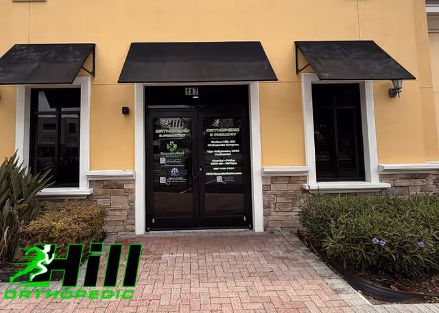 Front entrance of a yellow building with black awnings and a landscaped walkway.