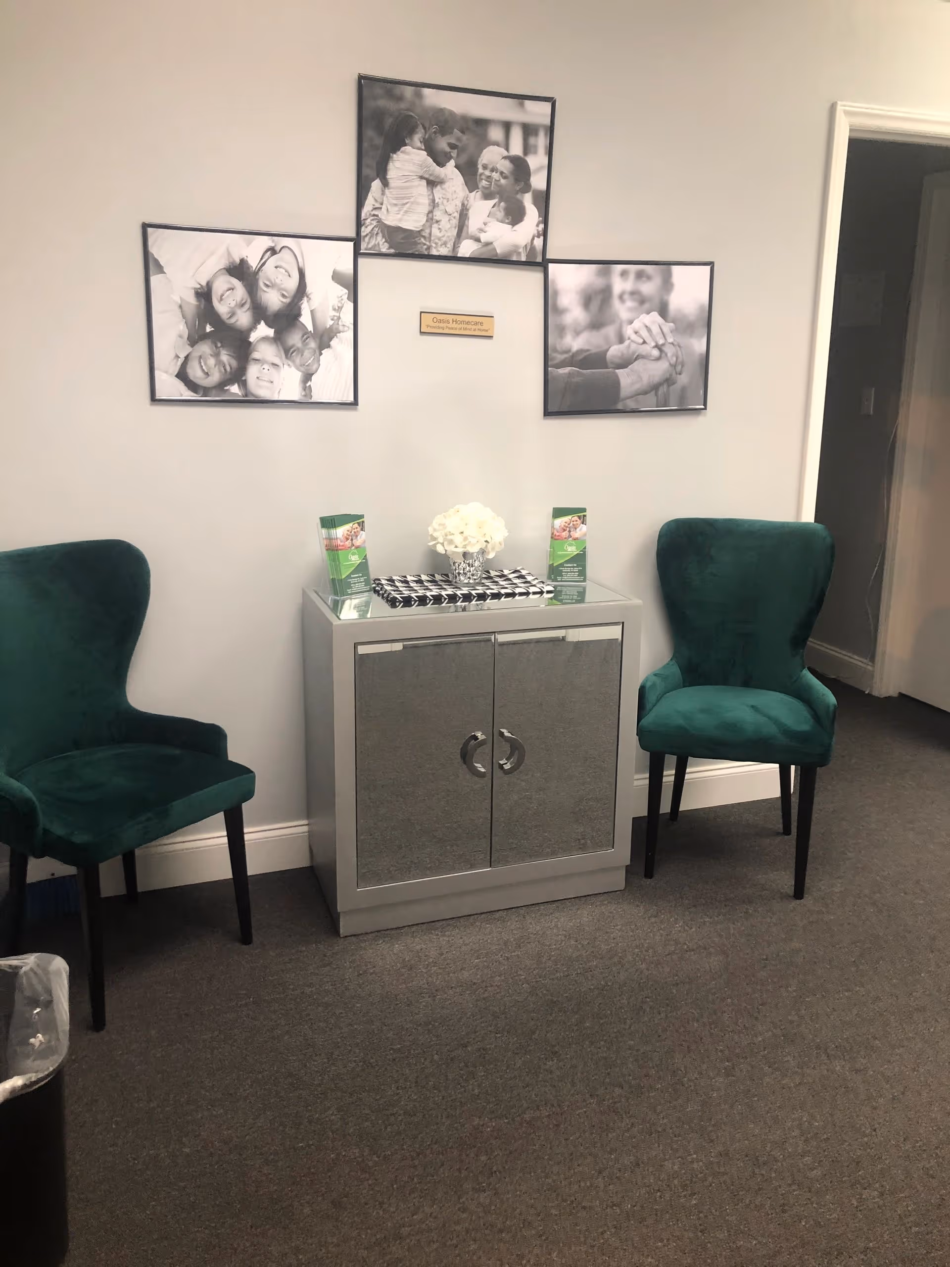 A small lobby area with two green chairs, a cabinet, and wall photo collage.
