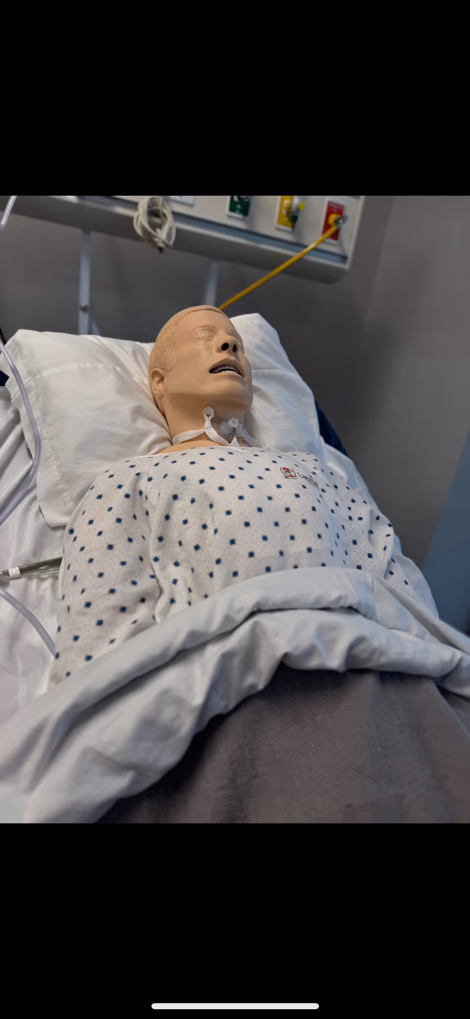 Medical mannequin resting in a hospital bed with a gown in a clinical room