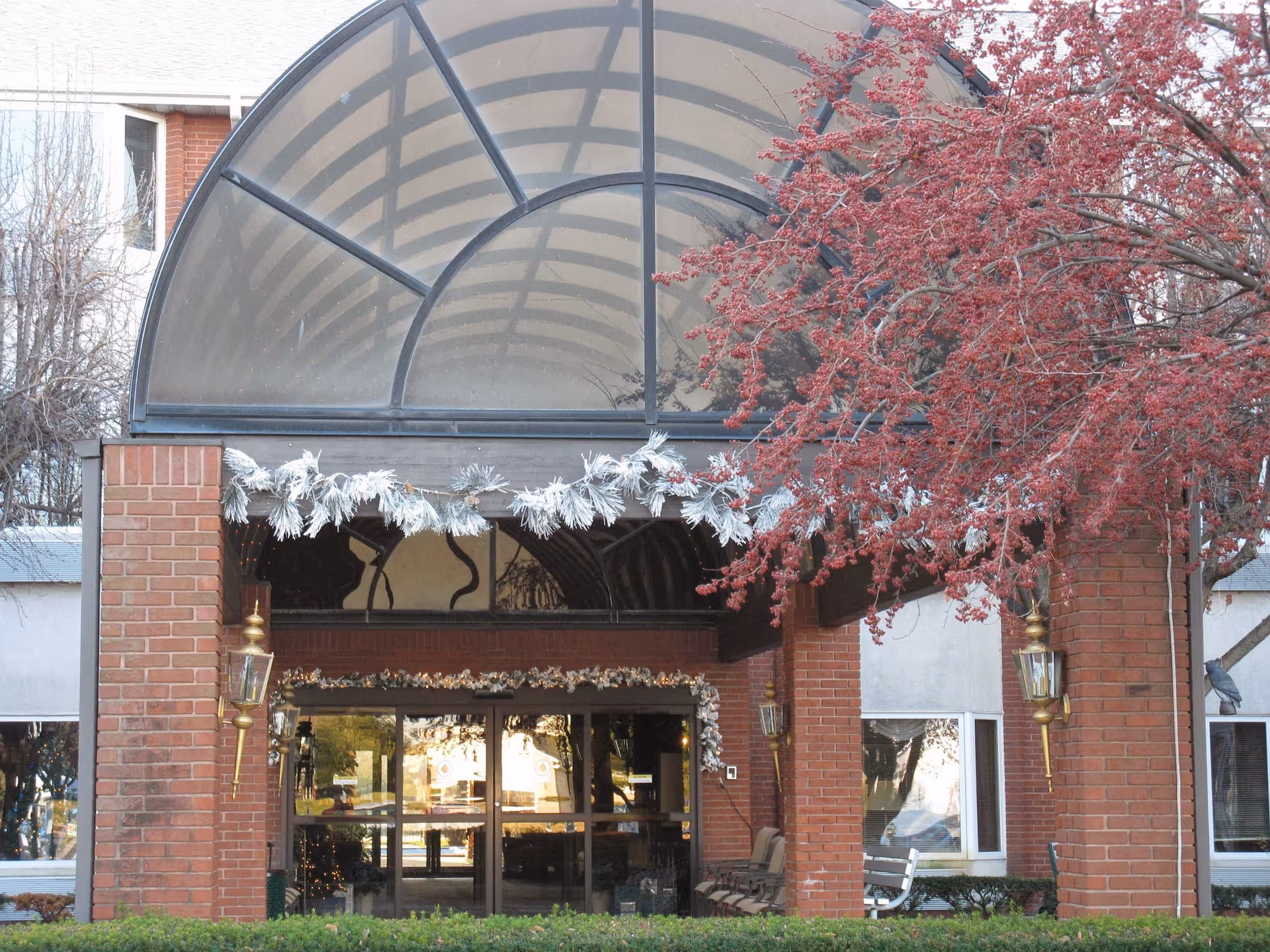 Brick senior living facility entrance with a glass canopy and festive garlands.