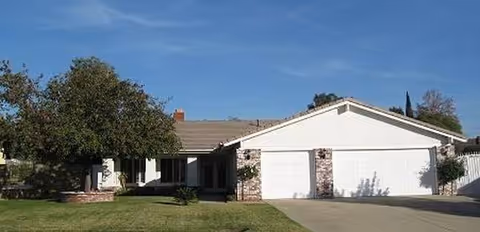 Single-story white residence with brick accents, three-car garage, front lawn and blue sky.