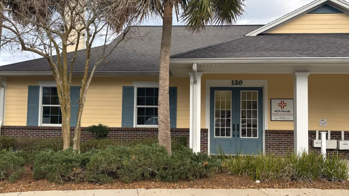 Yellow single-story facility exterior with blue doors, landscaping, and HCA Florida Healthcare at Home sign