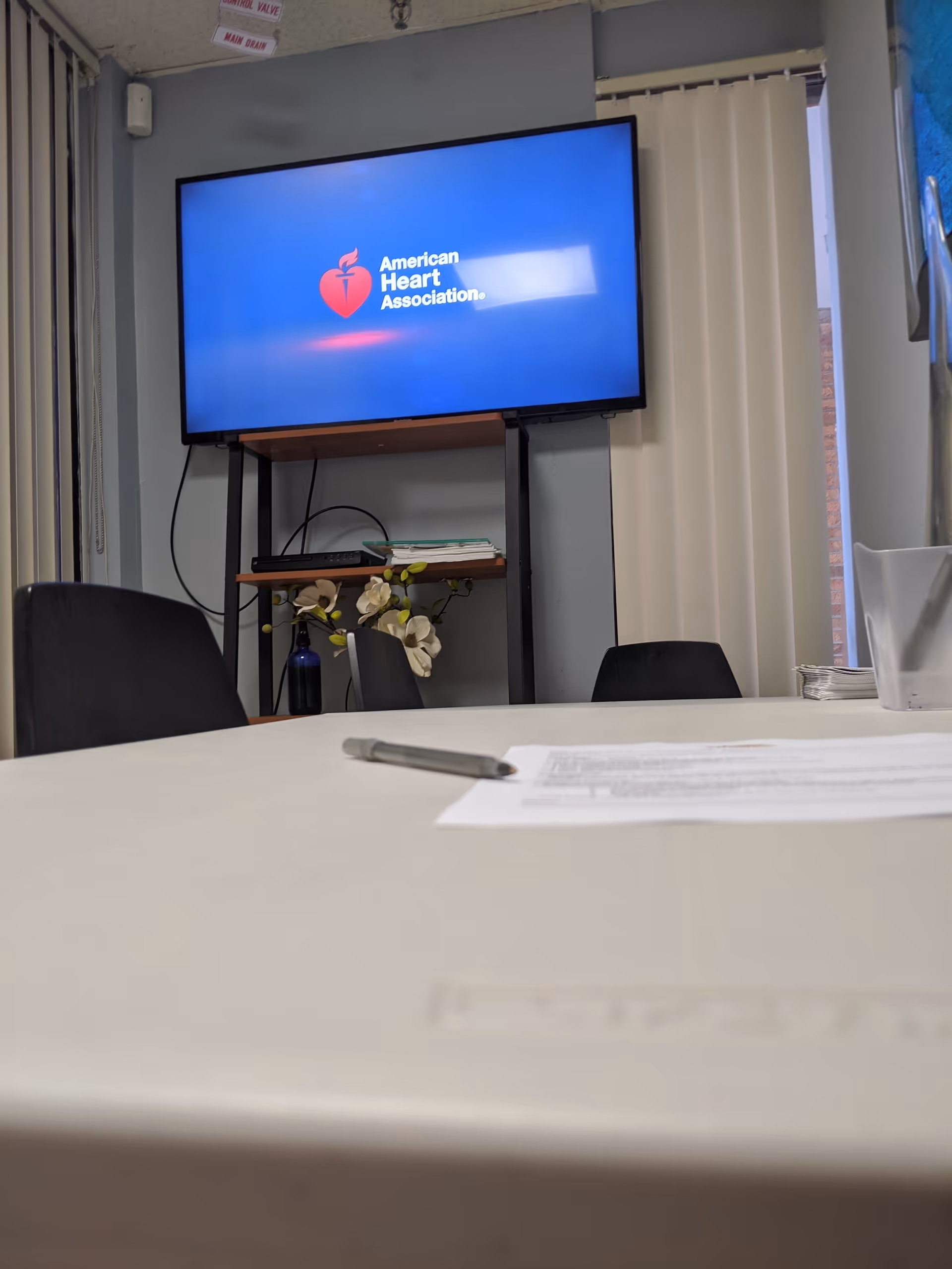 Conference room with table, papers, pen, chairs, and a TV screen displaying American Heart Association.