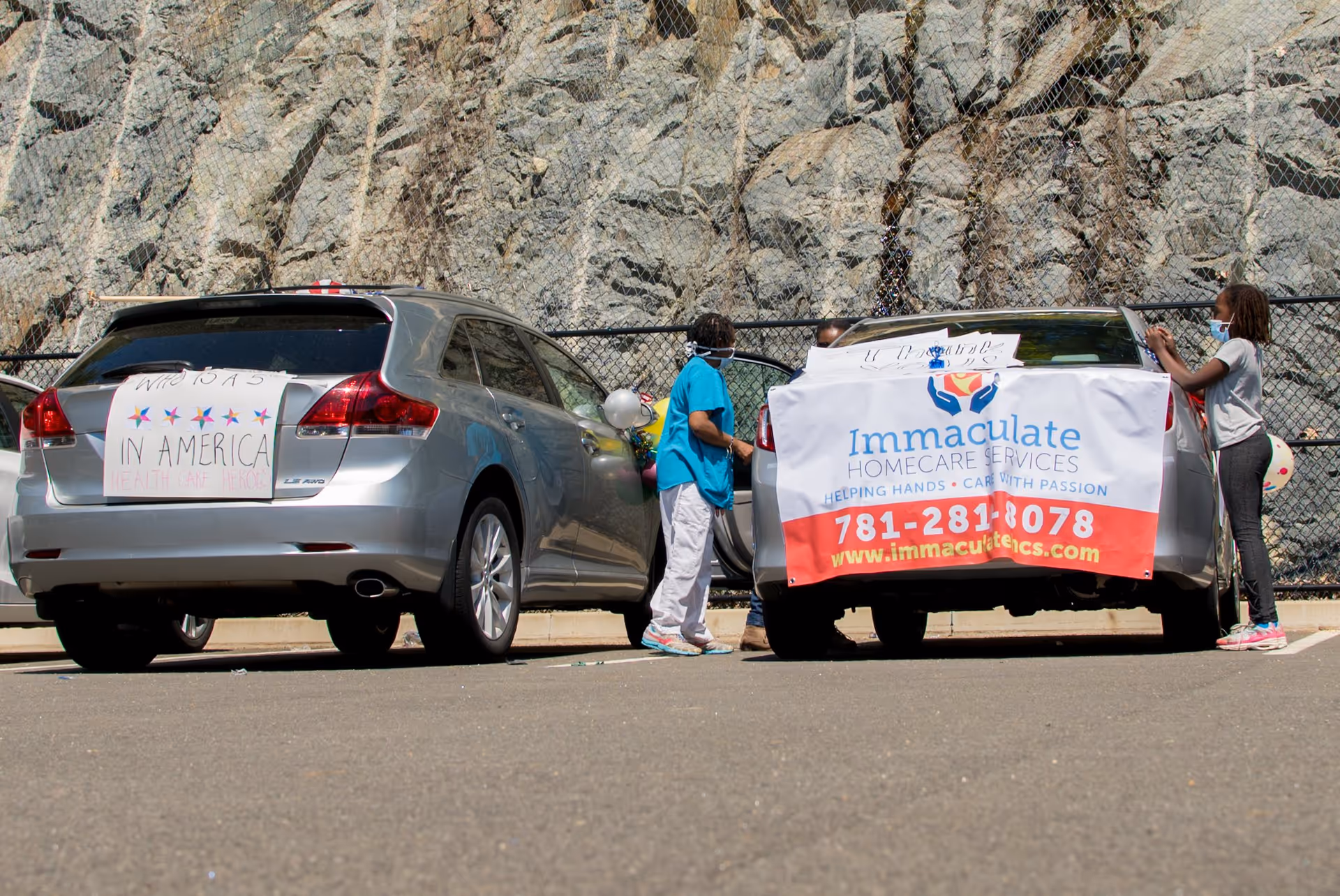 Drive-through event in parking lot with cars, volunteers, and Immaculate Homecare Services banner.