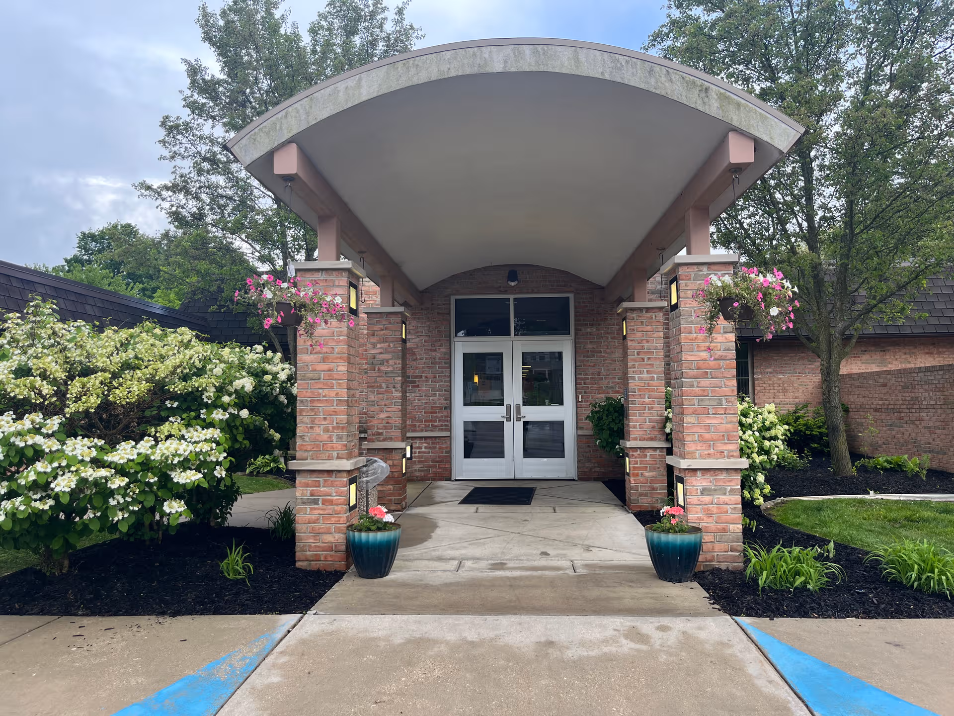 Entrance to Marshall Nursing & Rehab: brick building with curved canopy and flowering shrubs.