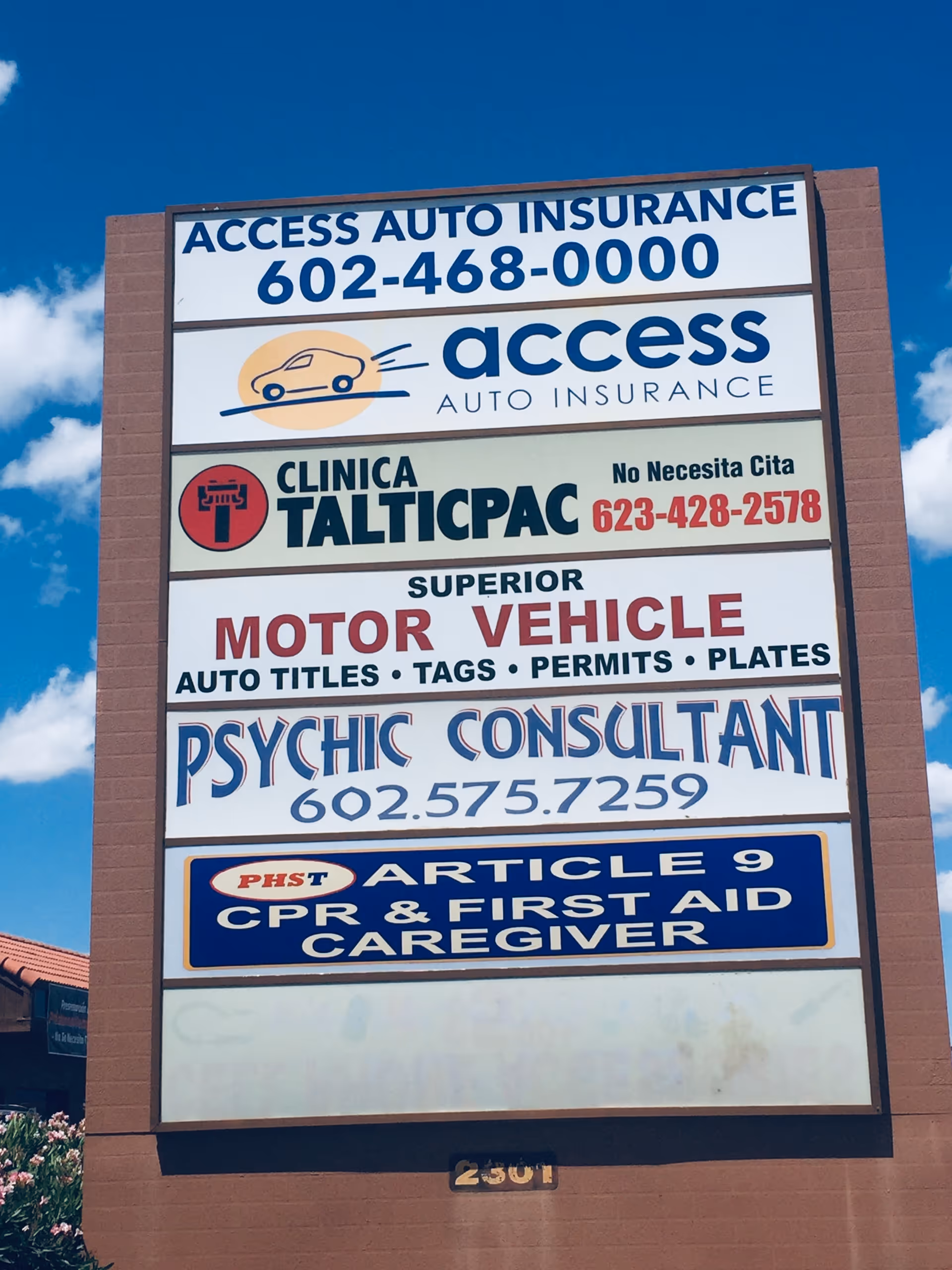 Tall outdoor sign on brick pillar displaying multiple business advertisements against blue sky