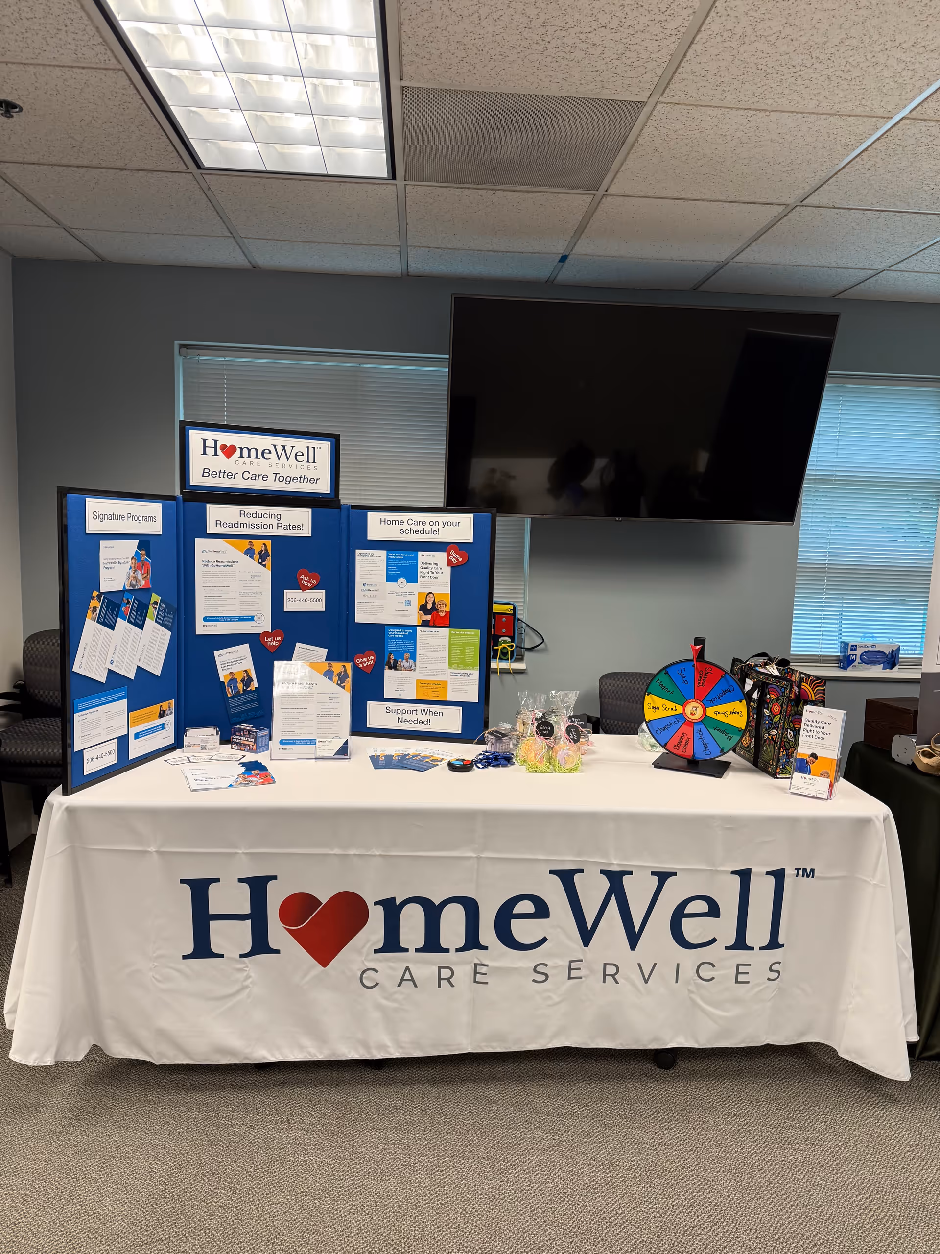Indoor information table with HomeWell branding, posters, and a spinning wheel display.
