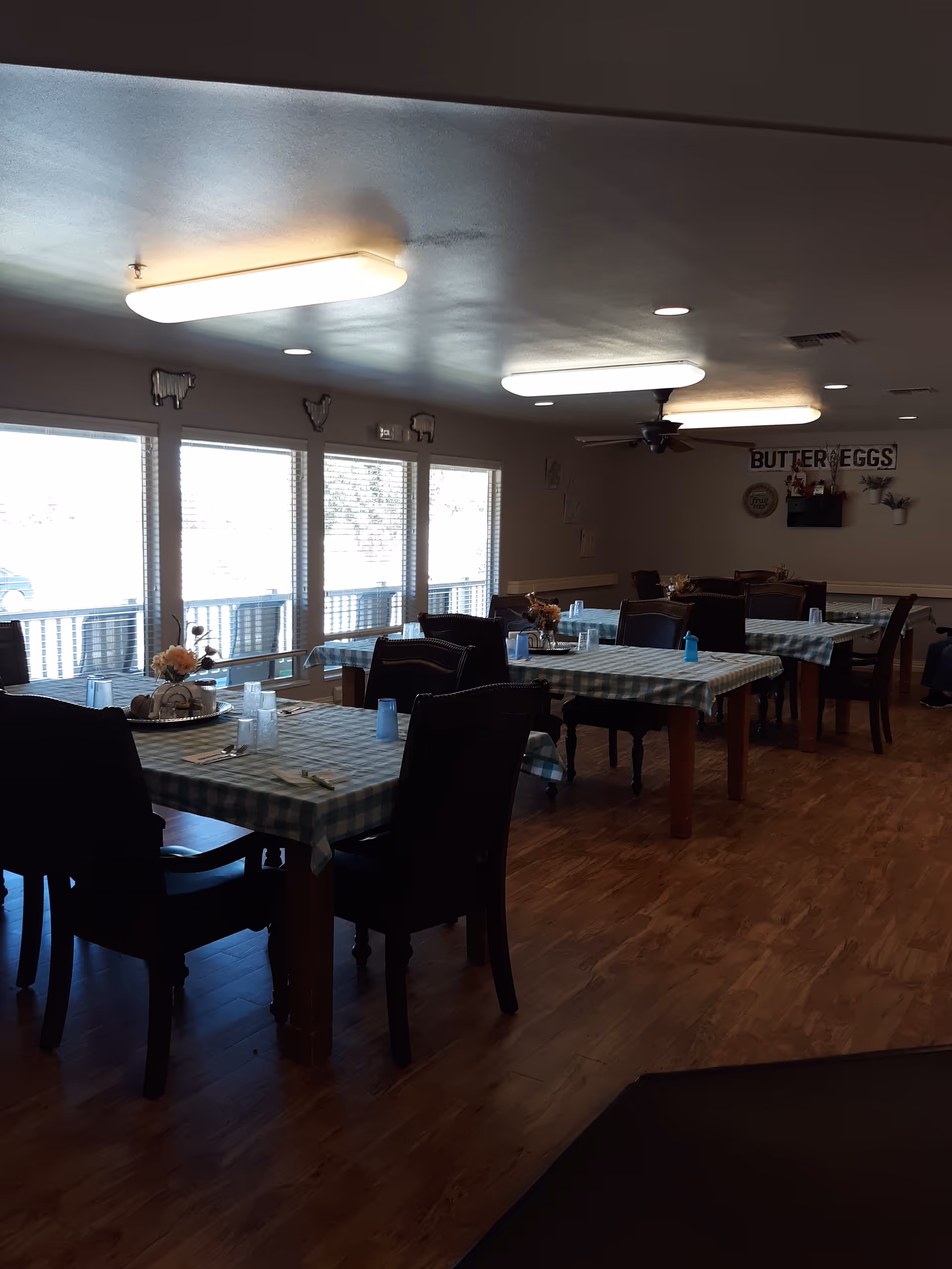 Spacious dining room with plaid tablecloths, dark chairs, and large windows.