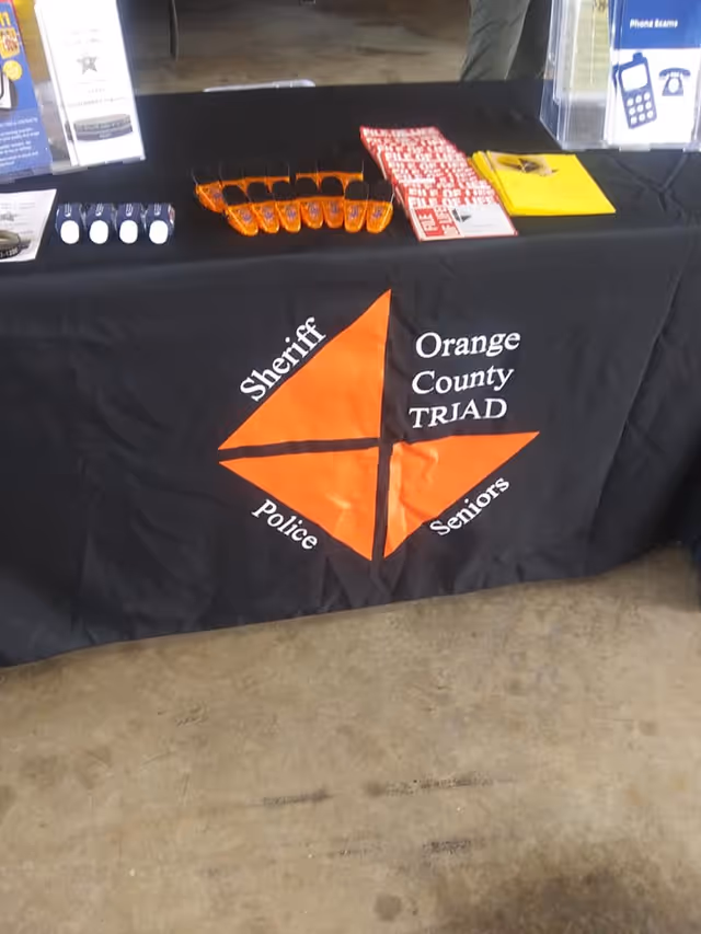 Table covered with black cloth displaying Orange County TRIAD logo and brochures at event.
