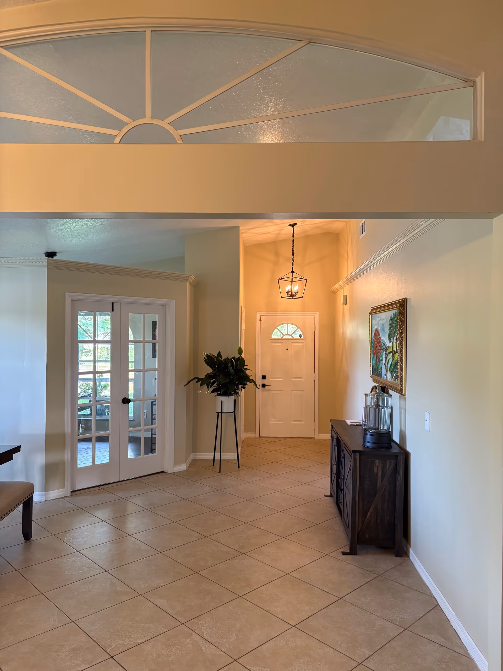 Bright entry hall with glass double doors, chandelier, plant, and console table.