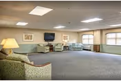 Spacious lounge with green upholstered seating, tables, lamps, and large windows.