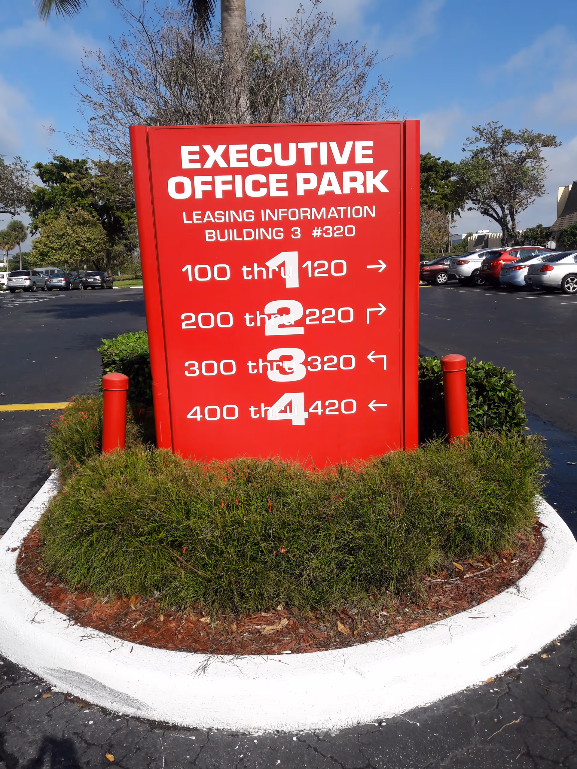 Bright red sign for Executive Office Park surrounded by bushes in a parking lot.