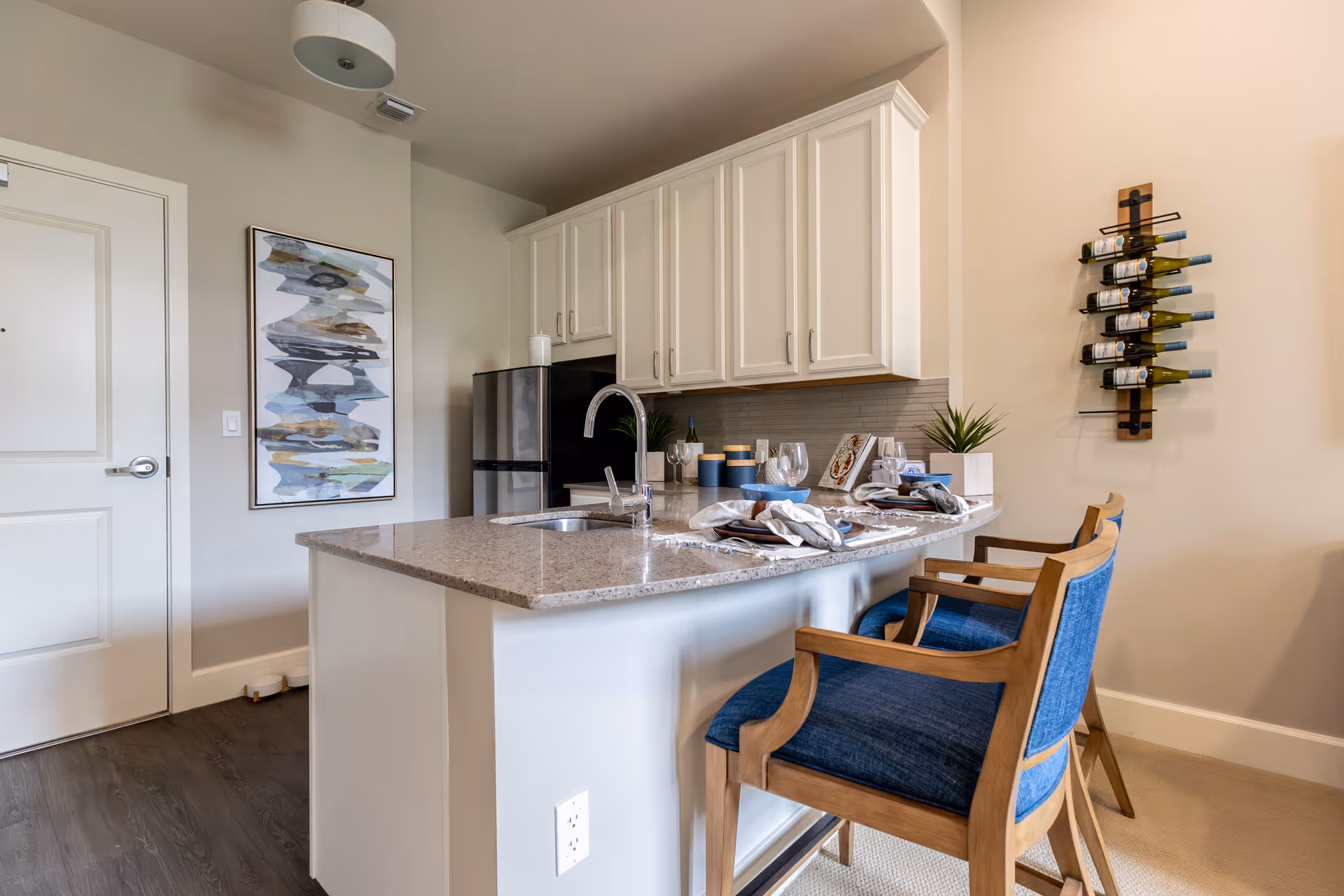 Modern kitchen with white cabinets, granite island, bar seating, wine rack, and decor.