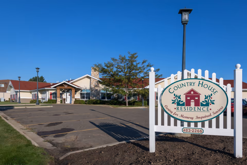 Exterior view of the Country House Residence building and parking lot with a prominent white sign in the foreground.