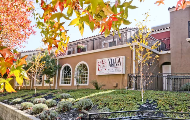 Exterior view of Villa Fontana Retirement Communities with sign, arched windows, and landscaped front yard.