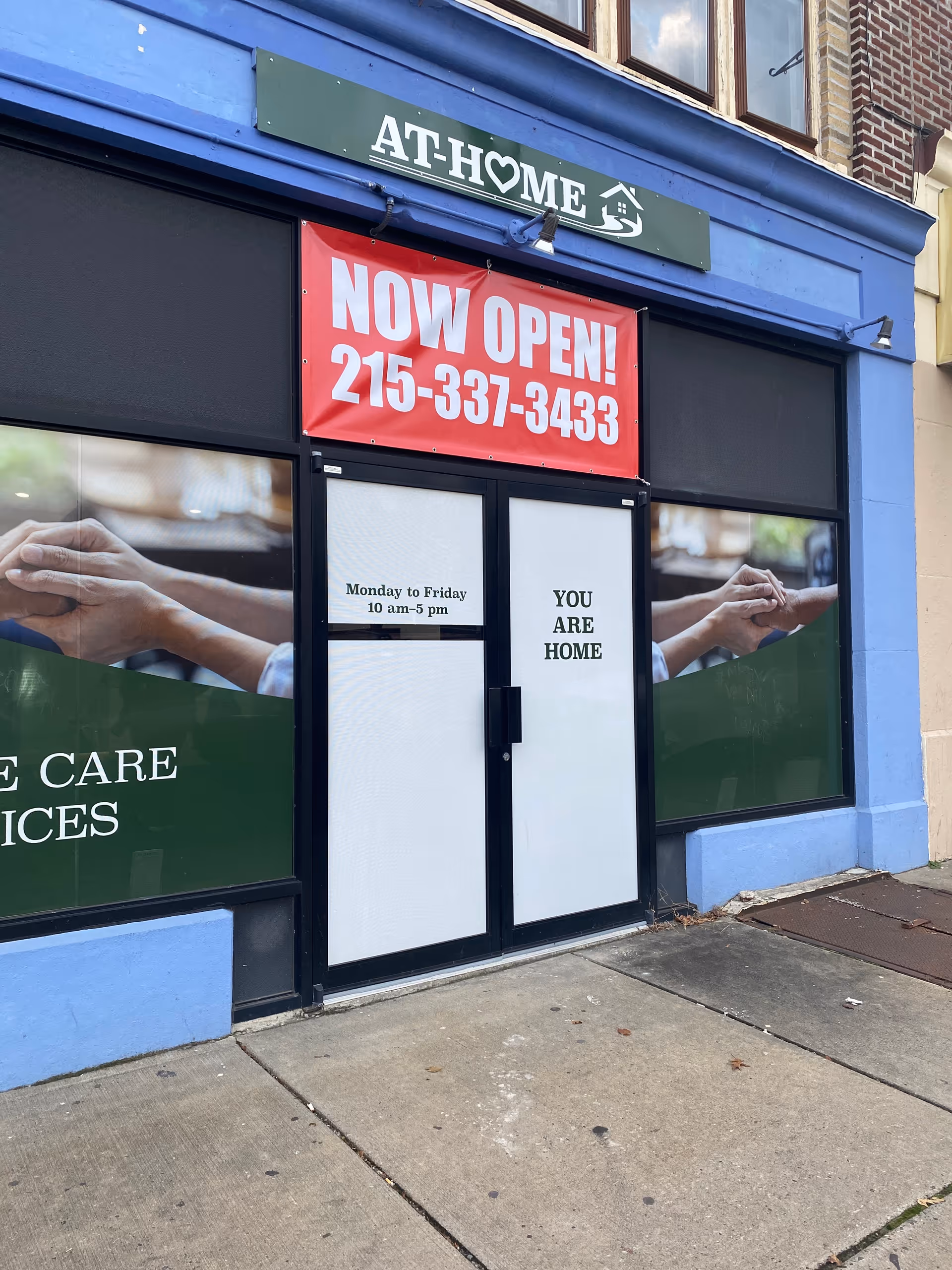 Exterior storefront for At Home Healthcare with a red Now Open banner and signage