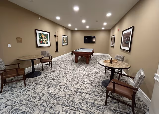 Recreation room with pool table, marble tables, chairs, wall art, and a TV on beige walls.