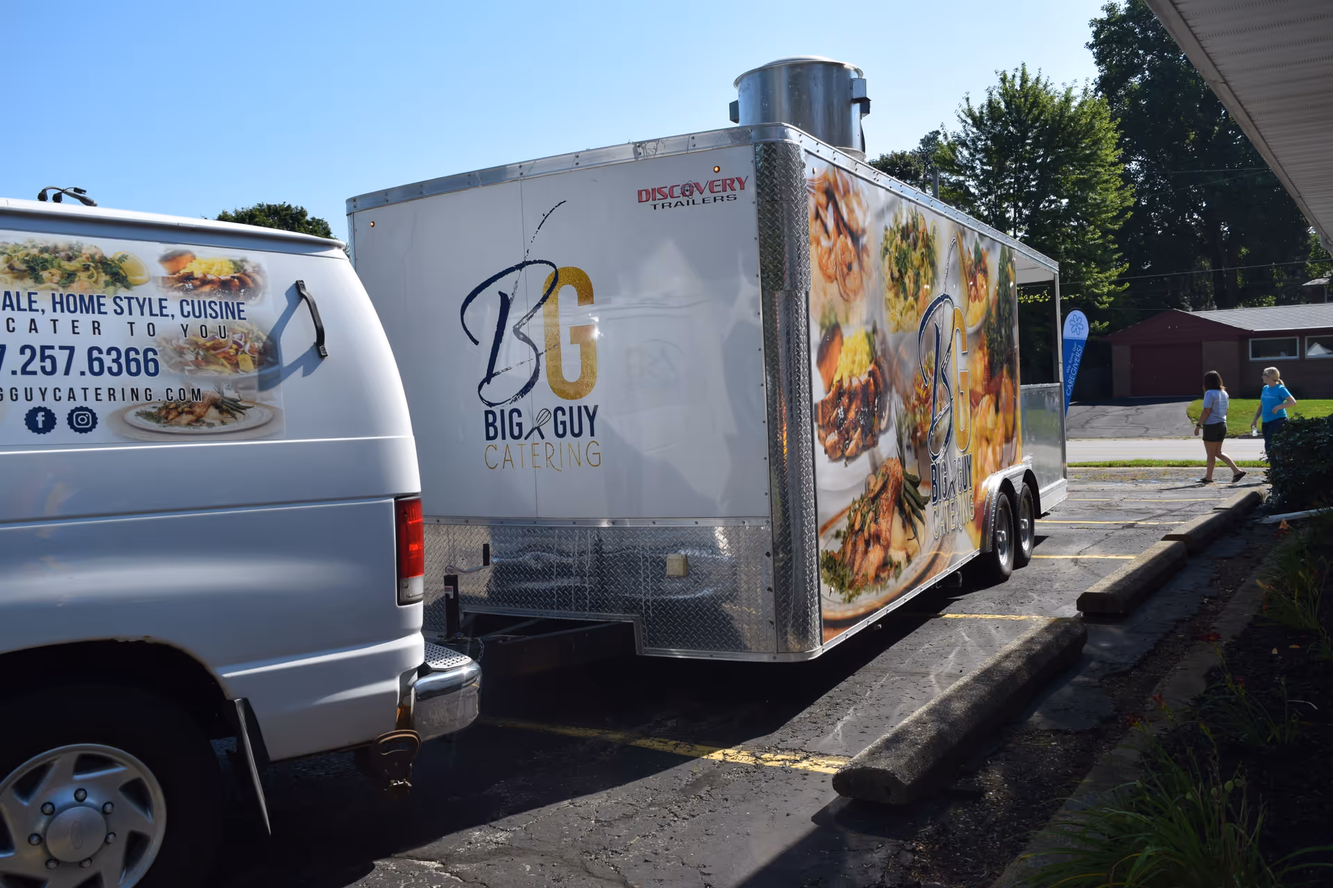 Outdoor parking lot with a catering trailer and a white van.