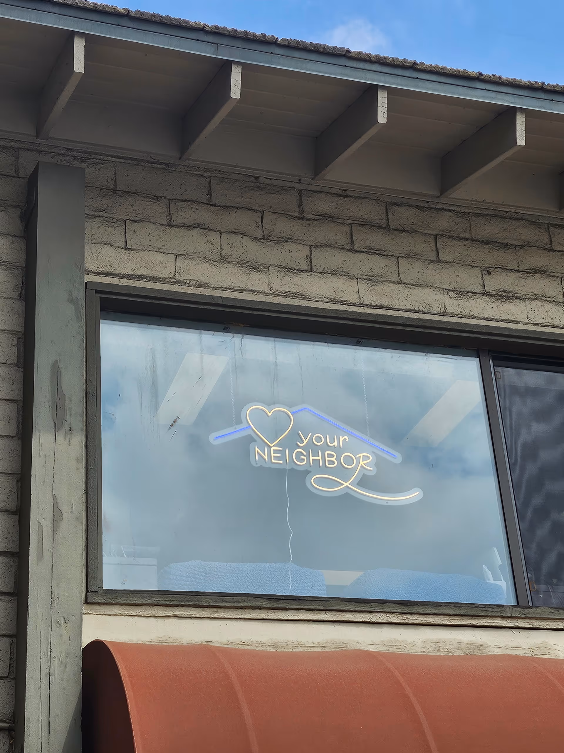 Building exterior with a window showing a neon sign reading your neighbor and a heart.
