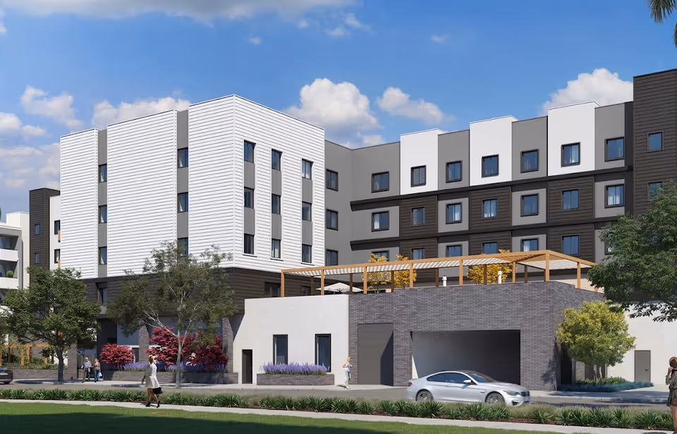 Modern multi-story senior living building with white and dark siding, a rooftop terrace, landscaping and a car parked in front.