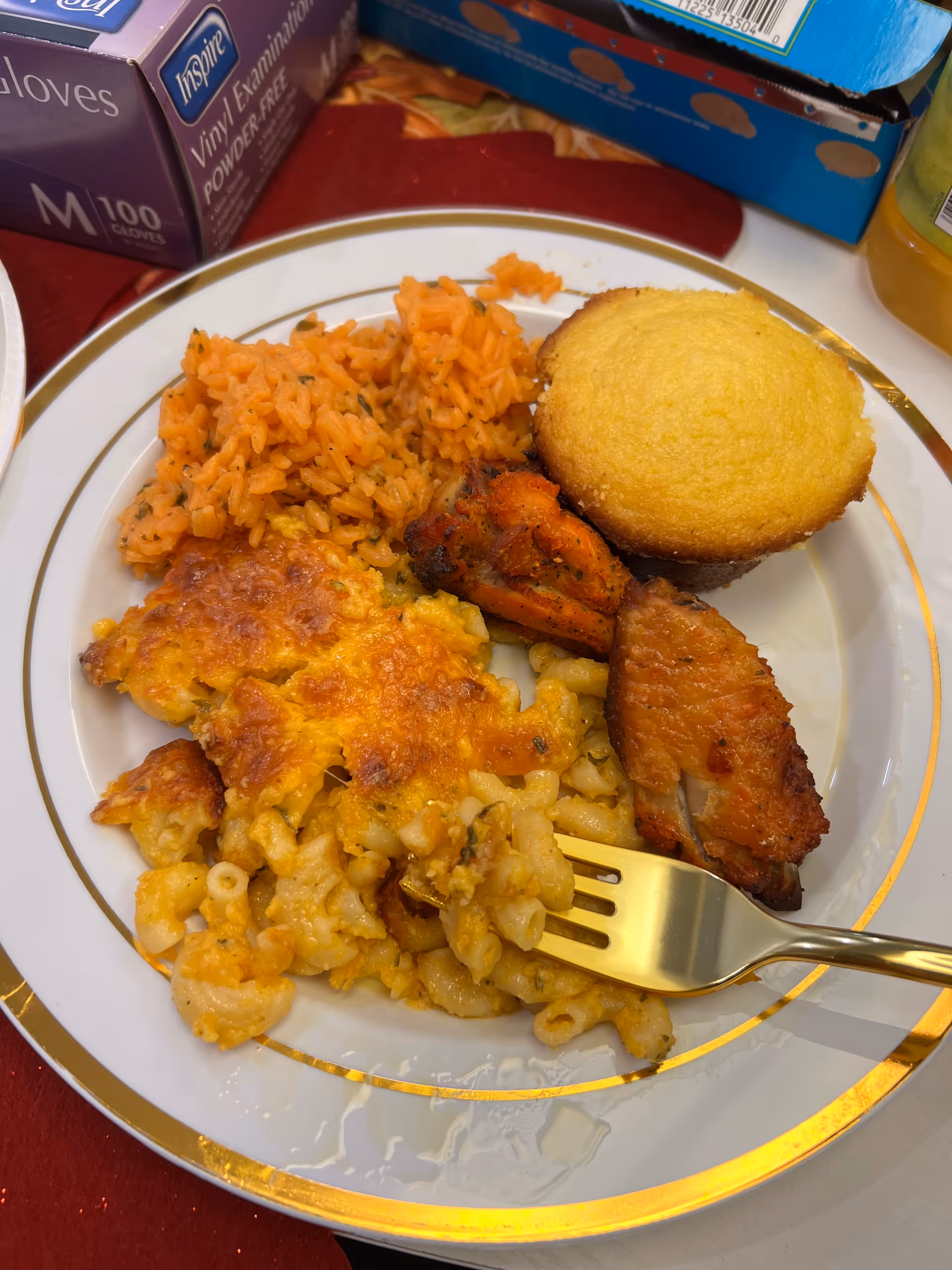 Plate of macaroni and cheese, cornbread, and meat on a table with boxed items in background.