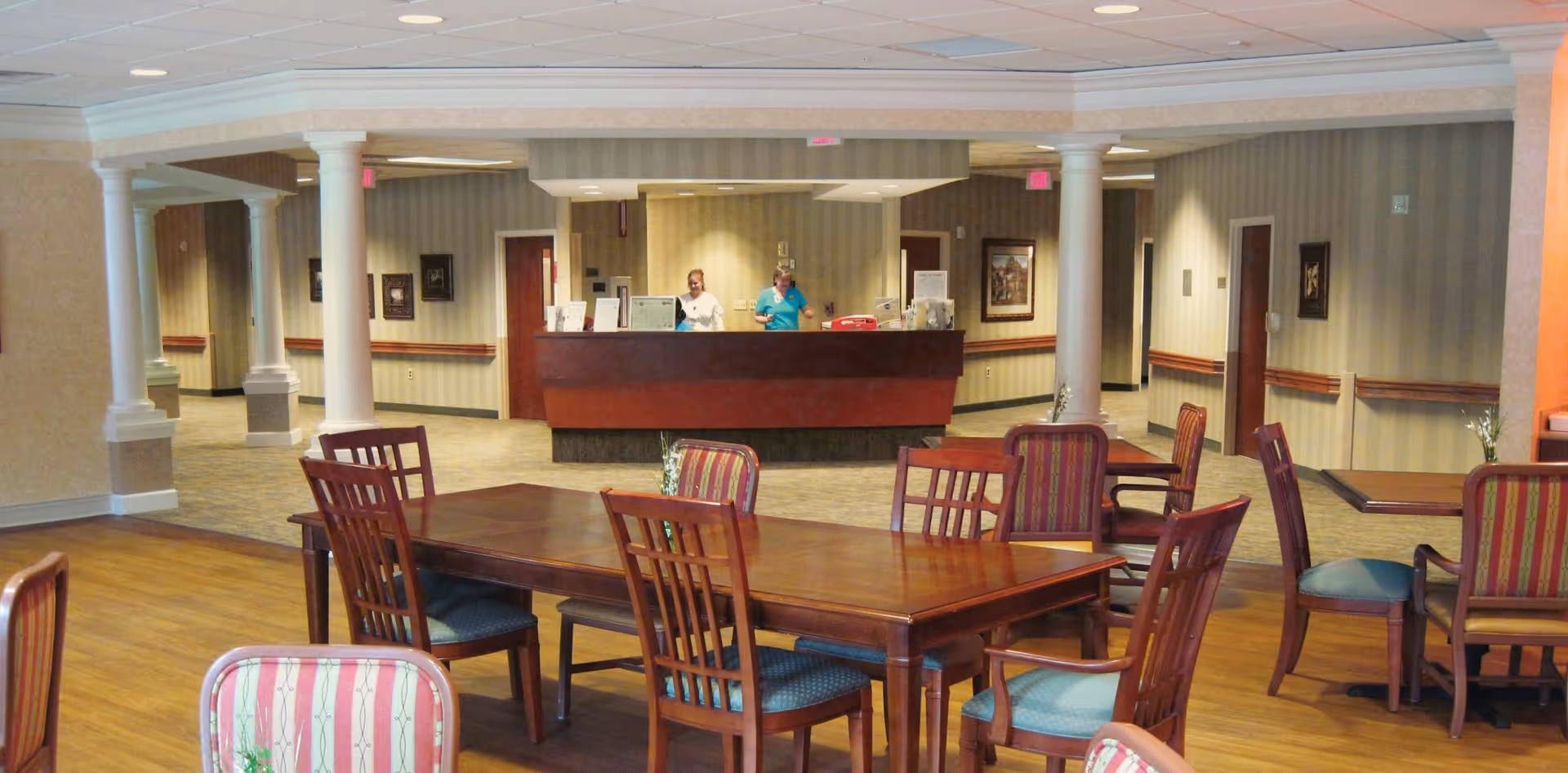 Interior common area with wooden dining tables and chairs, reception desk in background.
