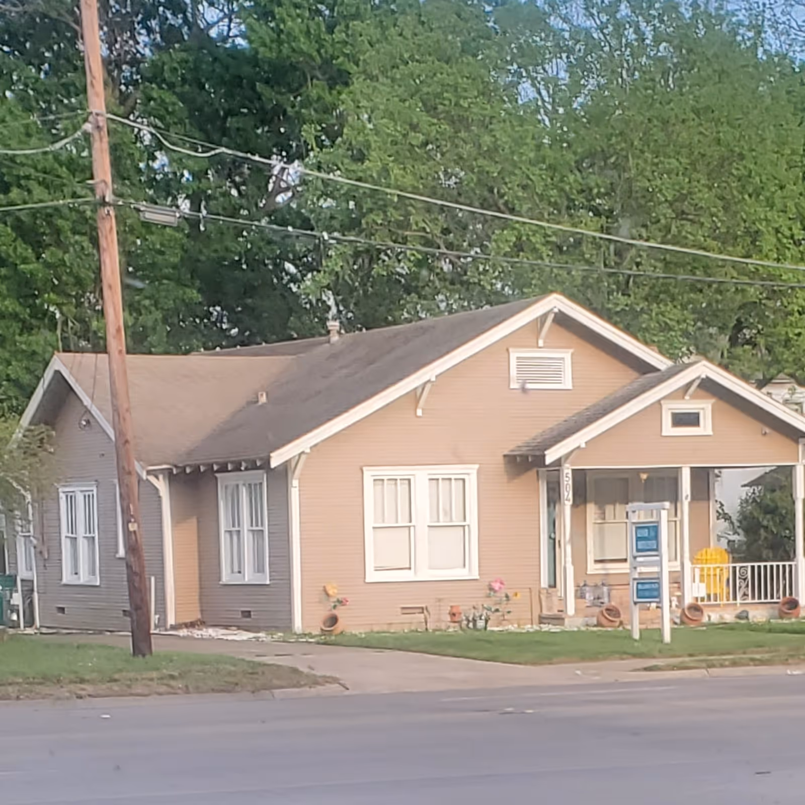 A small beige house with a front porch sits on a grassy street.