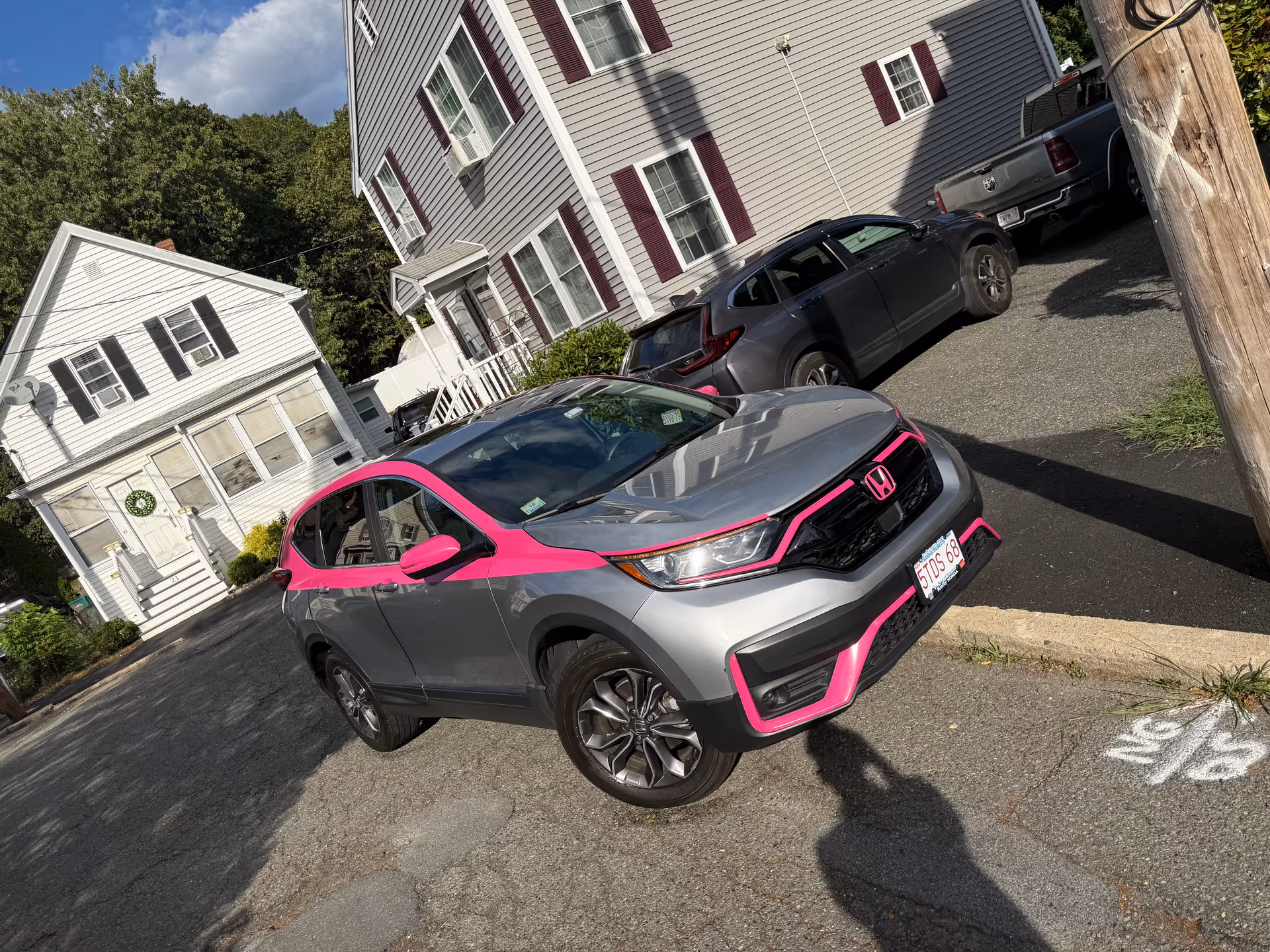 Exterior view of a two-story senior living building with parked cars, including a pink-trimmed gray Honda.